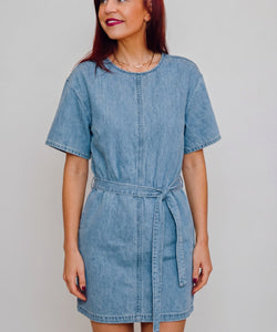 Model draagt een blauwe Bob & Bill Calle denim jurk met korte mouwen, ronde hals en strikceintuur in de taille.