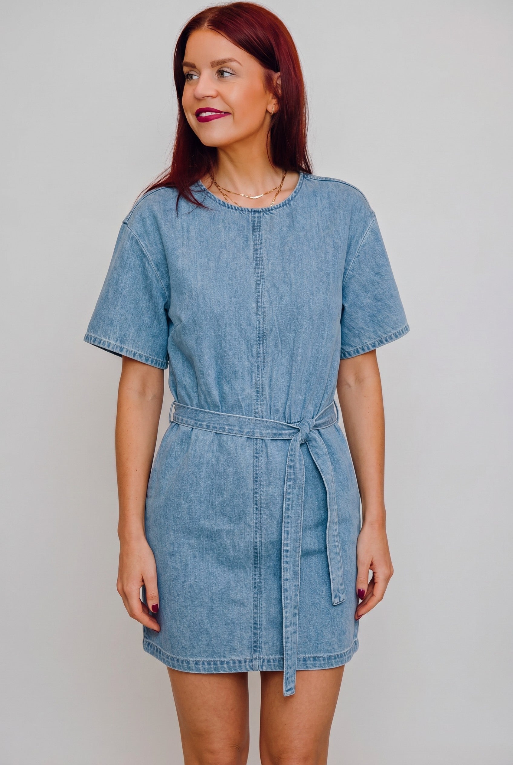 Model draagt een blauwe Bob & Bill Calle denim jurk met korte mouwen, ronde hals en strikceintuur in de taille.