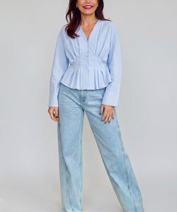 Model draagt Bob & Bill Emma blauwe katoenen blouse met v-hals, knoopsluiting en geplooid peplum effect.