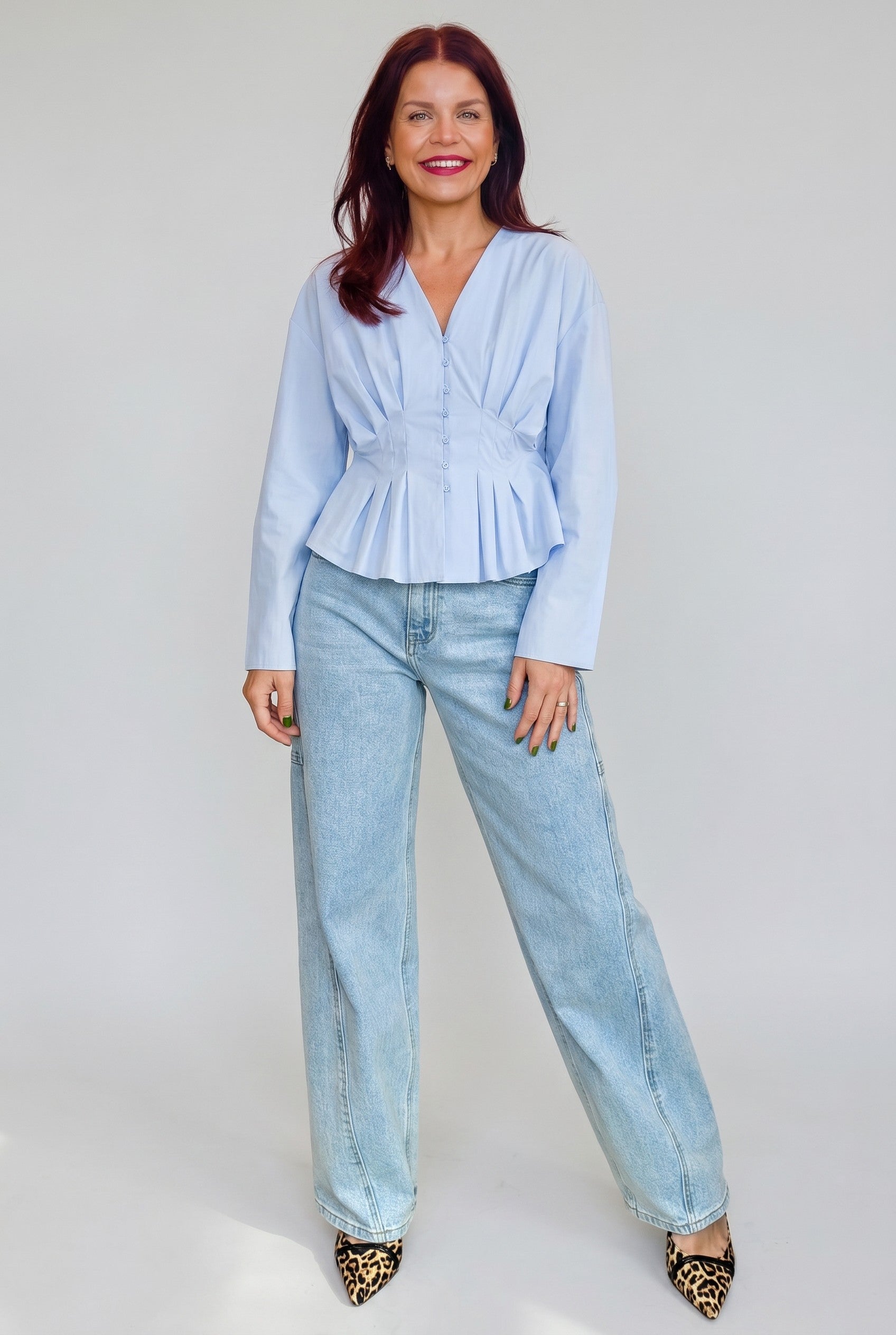 Model draagt Bob & Bill Emma blauwe katoenen blouse met v-hals, knoopsluiting en geplooid peplum effect.