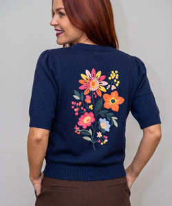 Bob & Bill navy knit sweater with short sleeves and vibrant floral embroidery on the back, worn by a woman.