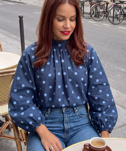 Bob & Bill navy polka dot blouse with long puff sleeves and high collar worn by a woman at a Parisian cafe table