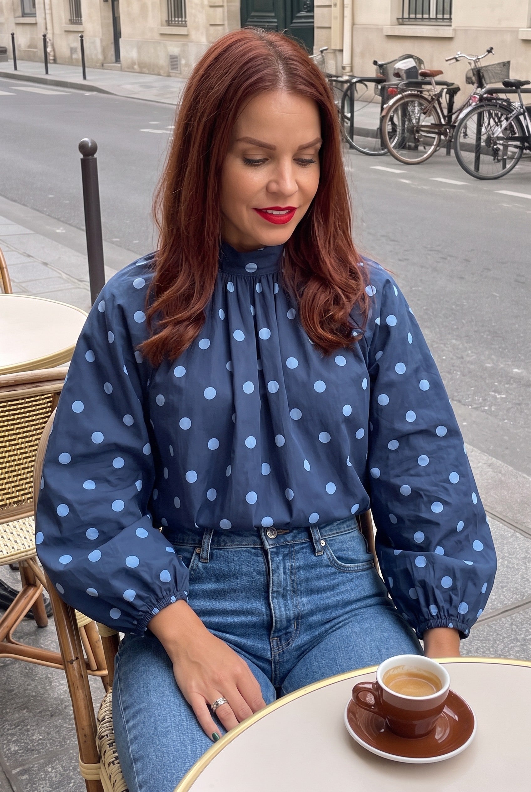 Bob & Bill navy polka dot blouse with long puff sleeves and high collar worn by a woman at a Parisian cafe table