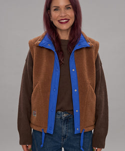 Bob & Bill reversible brown teddy gilet with royal blue trim and button closure worn by a smiling woman