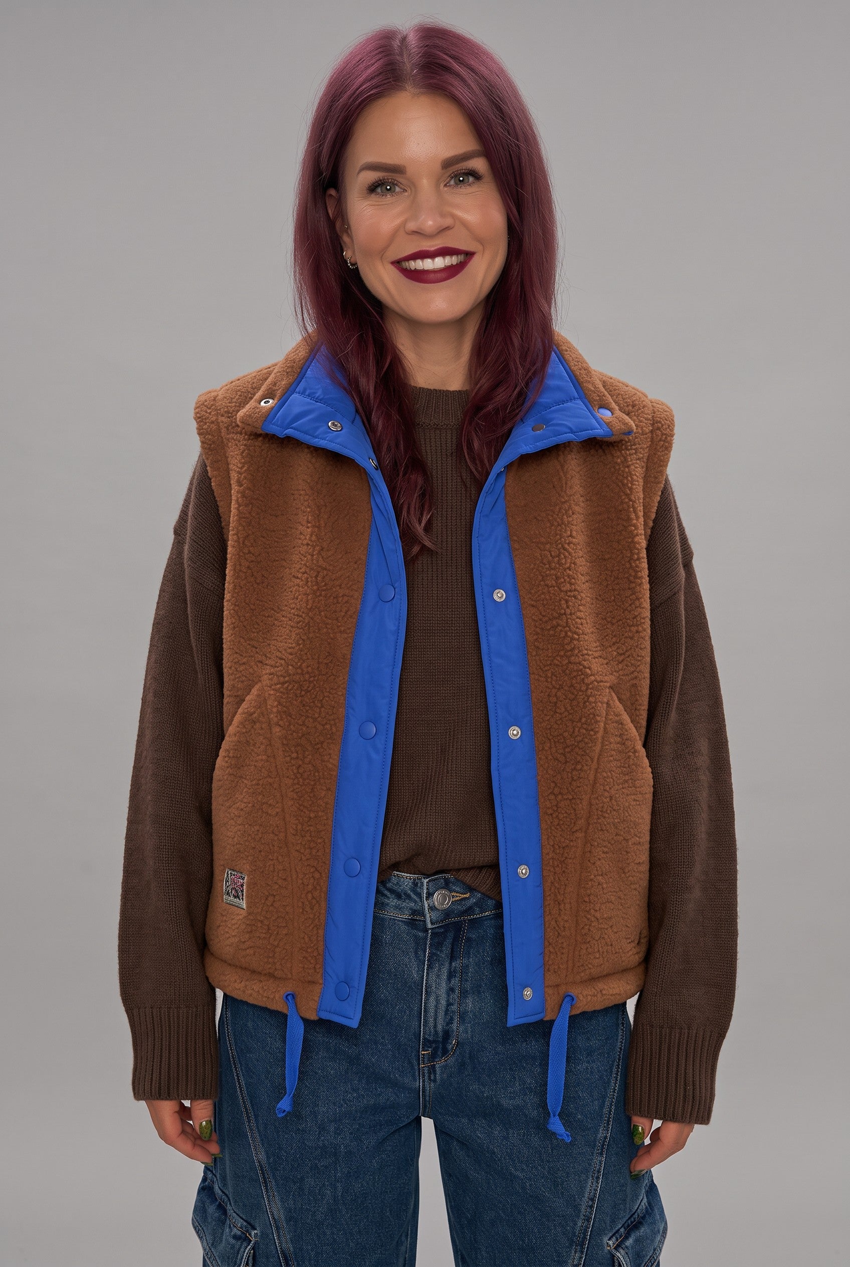 Bob & Bill reversible brown teddy gilet with royal blue trim and button closure worn by a smiling woman